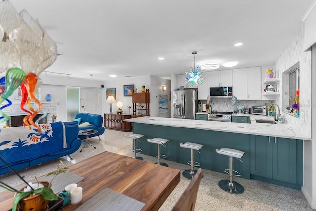 kitchen featuring kitchen peninsula, sink, appliances with stainless steel finishes, decorative light fixtures, and white cabinetry