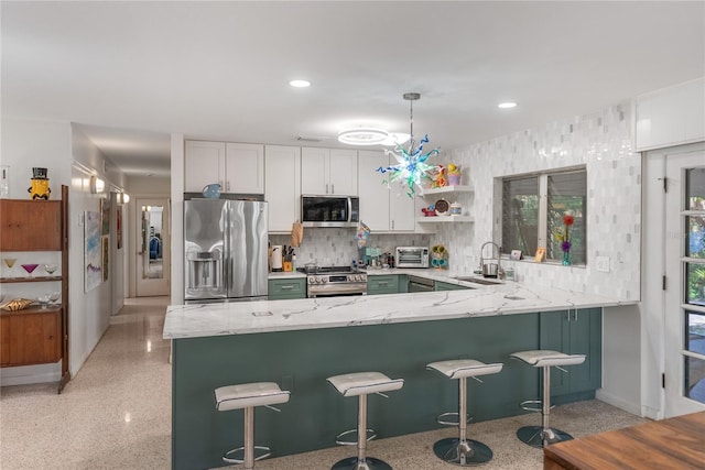 kitchen featuring pendant lighting, white cabinets, appliances with stainless steel finishes, a kitchen bar, and kitchen peninsula