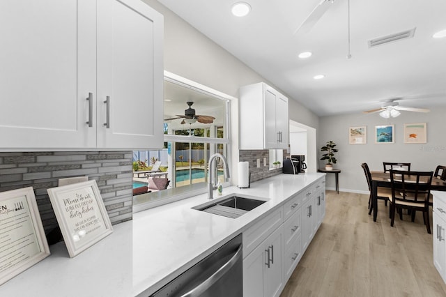 kitchen with light wood-type flooring, backsplash, stainless steel dishwasher, sink, and white cabinets