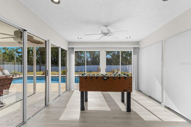 recreation room featuring ceiling fan, light wood-type flooring, and a textured ceiling