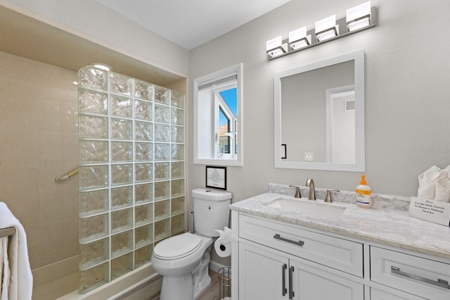 bathroom featuring a tile shower, vanity, and toilet