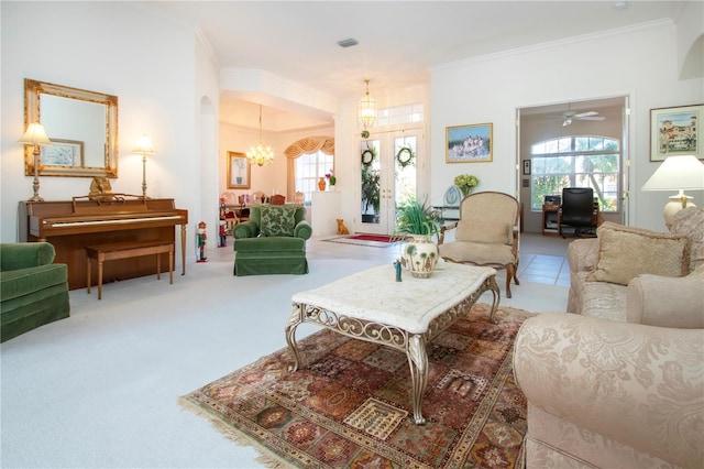 carpeted living room featuring french doors, ceiling fan with notable chandelier, and crown molding