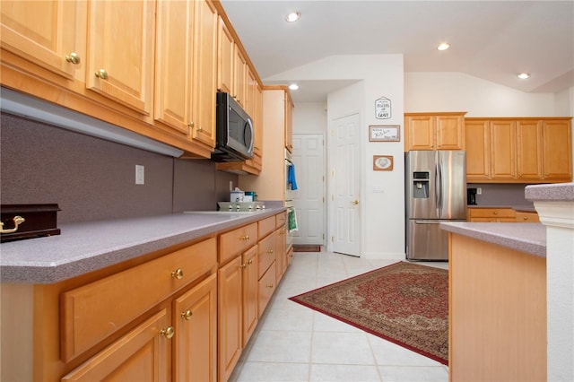 kitchen with light tile patterned flooring, lofted ceiling, light brown cabinetry, and appliances with stainless steel finishes