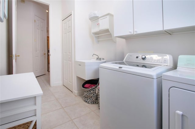 clothes washing area with cabinets, light tile patterned floors, and washing machine and dryer