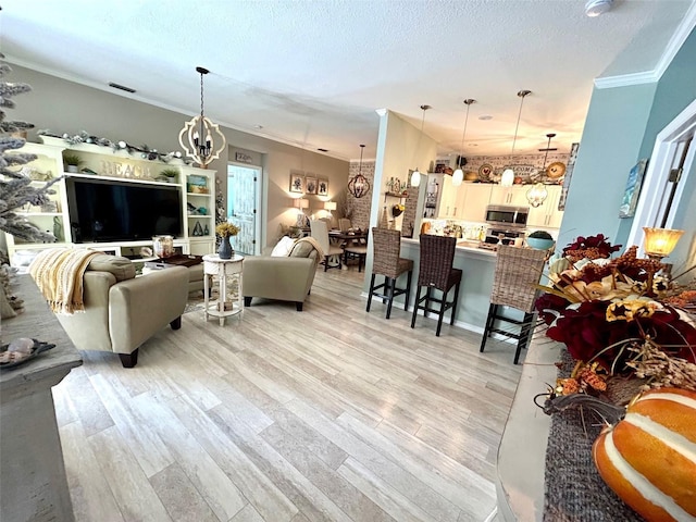 living room with a textured ceiling, light wood-type flooring, crown molding, and a notable chandelier