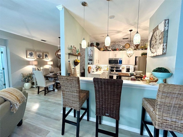 kitchen with white cabinetry, stainless steel appliances, kitchen peninsula, pendant lighting, and a kitchen bar