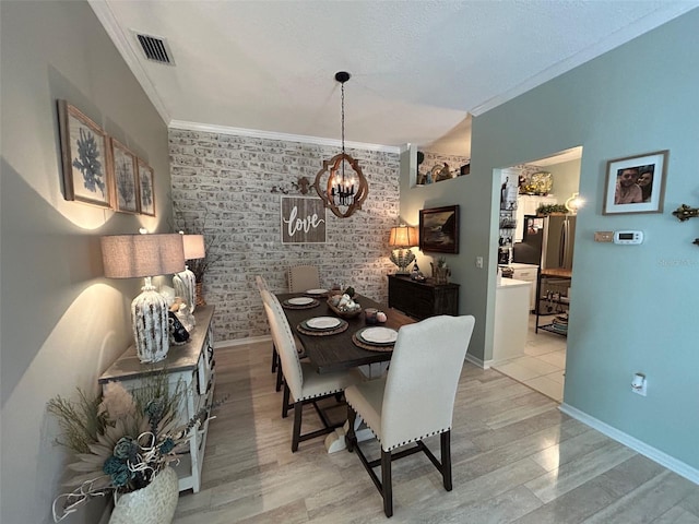 dining room featuring crown molding, brick wall, light wood-type flooring, and an inviting chandelier