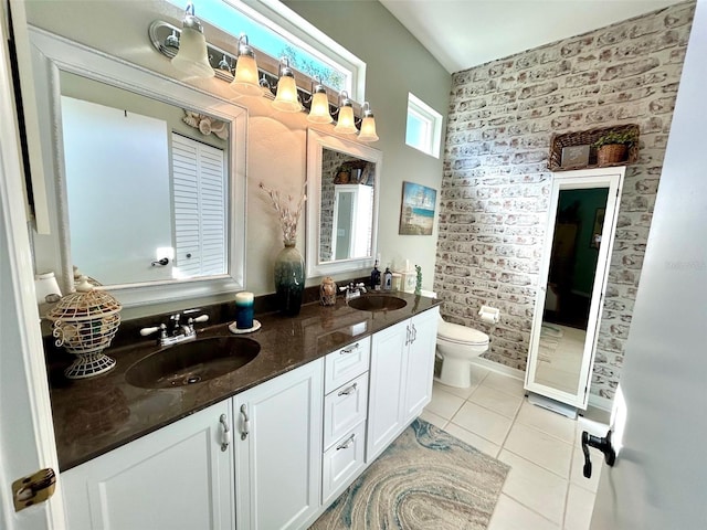 bathroom featuring tile patterned flooring, vanity, toilet, and brick wall