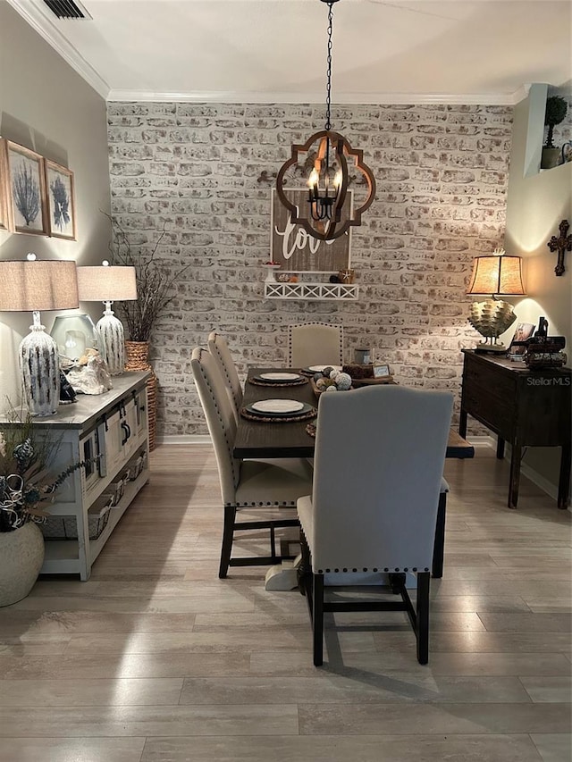 dining space with visible vents, brick wall, wood finished floors, crown molding, and a chandelier