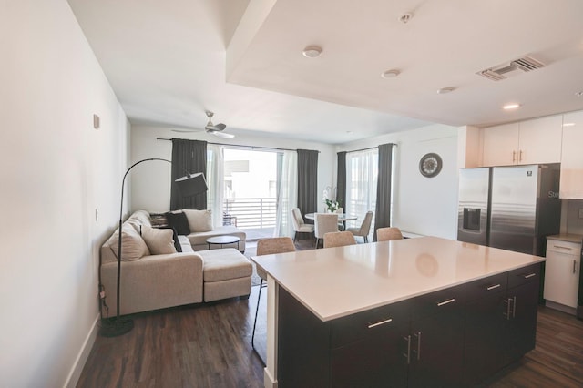 kitchen featuring stainless steel fridge, a kitchen island, ceiling fan, dark wood-type flooring, and white cabinetry