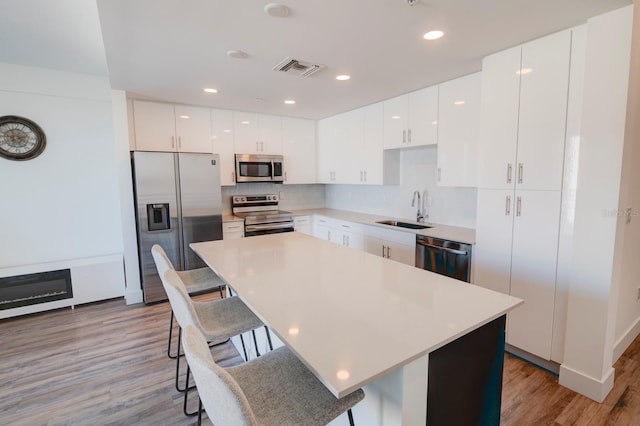 kitchen featuring sink, stainless steel appliances, light hardwood / wood-style floors, a breakfast bar area, and white cabinets