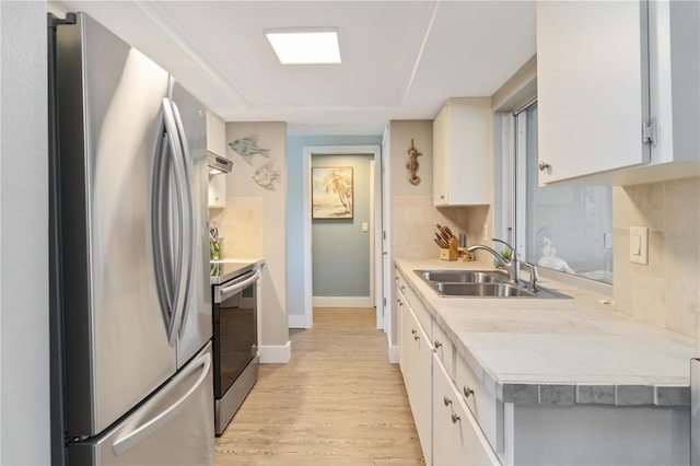 kitchen with sink, appliances with stainless steel finishes, tasteful backsplash, white cabinets, and light wood-type flooring