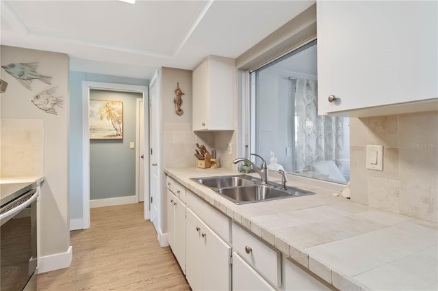 kitchen featuring sink, white cabinetry, tile countertops, light hardwood / wood-style flooring, and backsplash