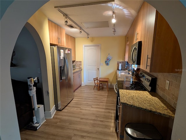 kitchen featuring light wood-type flooring, rail lighting, backsplash, stainless steel appliances, and stone countertops