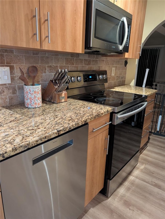 kitchen featuring decorative backsplash, light stone counters, light wood-type flooring, and stainless steel appliances