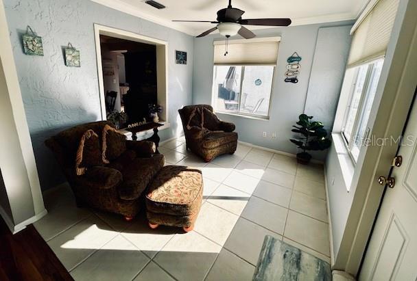 living area featuring light tile patterned floors, crown molding, a wealth of natural light, and ceiling fan