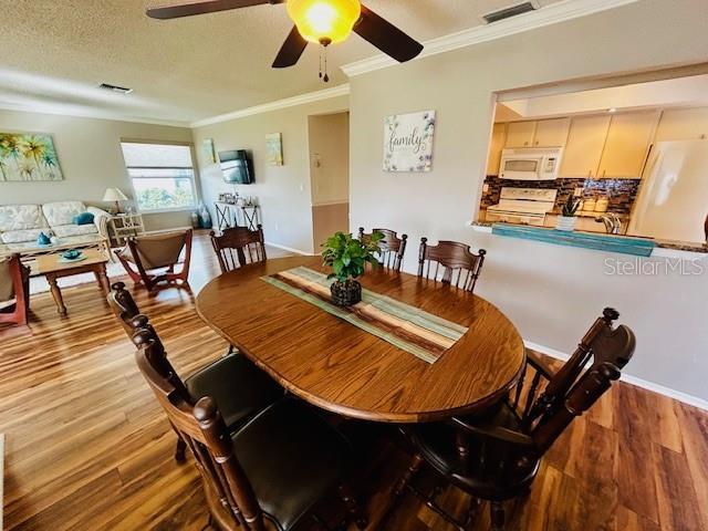 dining room with wood-type flooring, crown molding, a textured ceiling, and ceiling fan