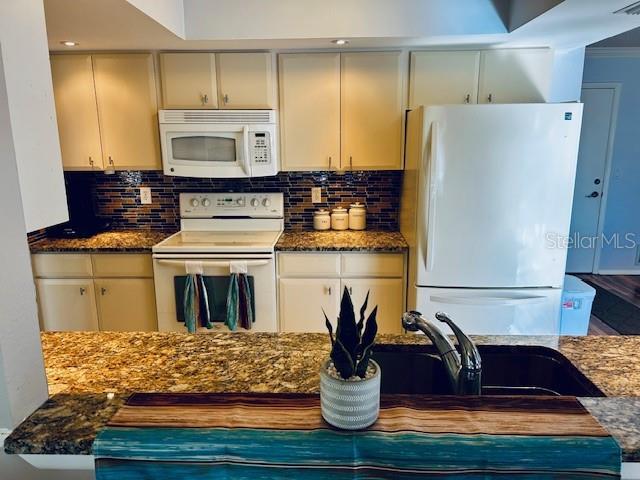 kitchen with sink, white appliances, dark stone counters, and decorative backsplash