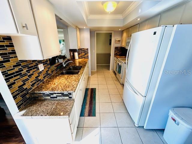 kitchen featuring stone countertops, sink, white cabinets, a tray ceiling, and white appliances