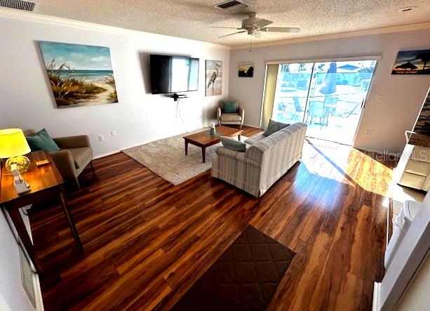 living room with ceiling fan, crown molding, dark wood-type flooring, and a textured ceiling