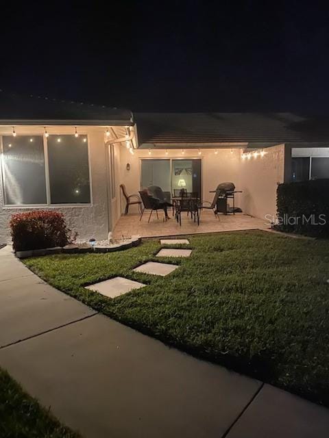 back house at twilight featuring a yard and a patio