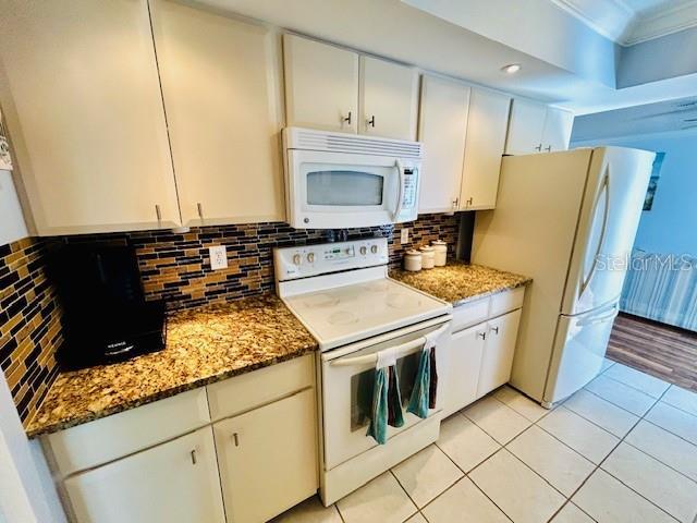 kitchen featuring white appliances, dark stone counters, and white cabinets