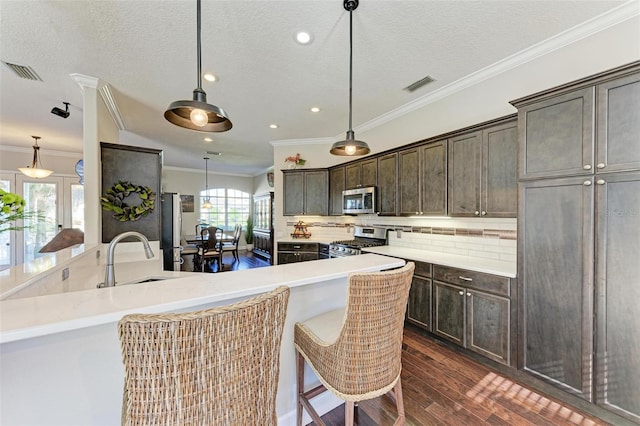 kitchen featuring appliances with stainless steel finishes, a breakfast bar, a textured ceiling, decorative light fixtures, and dark hardwood / wood-style floors