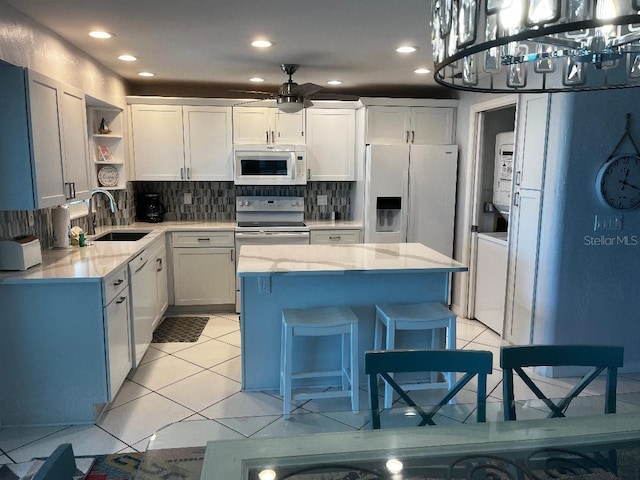 kitchen with white appliances, sink, light tile patterned floors, white cabinets, and a kitchen island