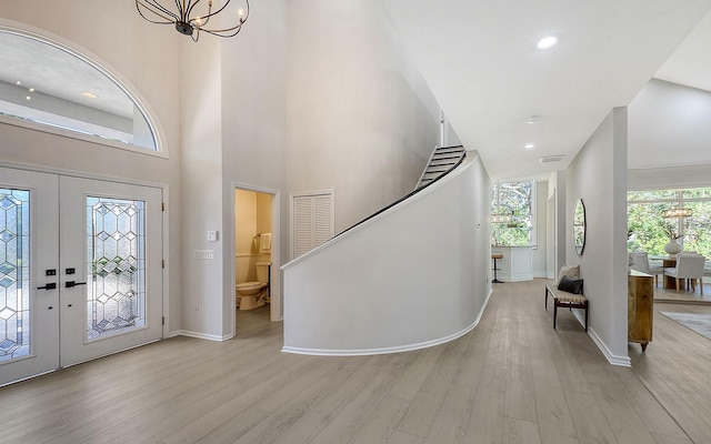 entryway with french doors, a towering ceiling, light hardwood / wood-style floors, and an inviting chandelier