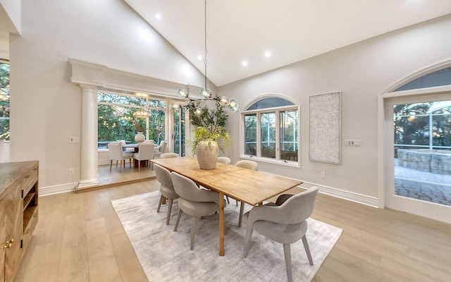 dining space with an inviting chandelier, light hardwood / wood-style flooring, high vaulted ceiling, and decorative columns