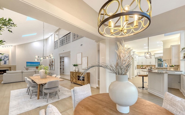 dining area with an inviting chandelier, a towering ceiling, and light wood-type flooring