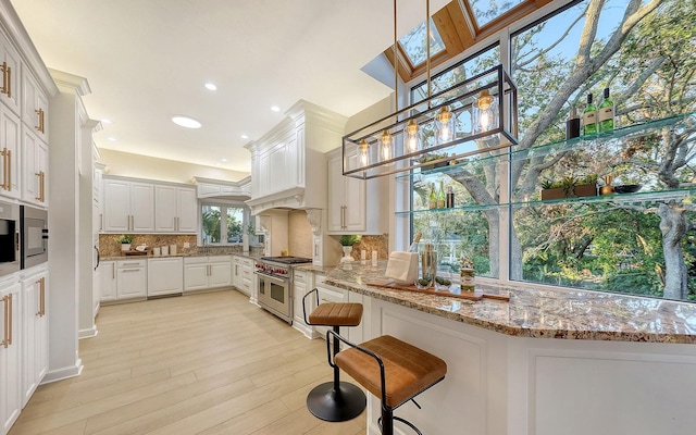 kitchen with double oven range, a skylight, tasteful backsplash, decorative light fixtures, and light hardwood / wood-style floors