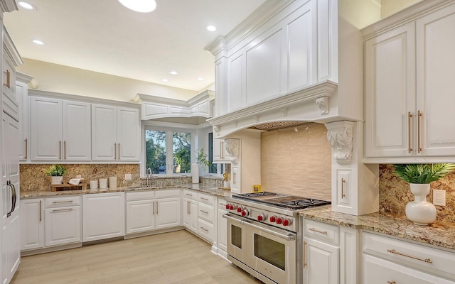 kitchen featuring double oven range, backsplash, white cabinets, sink, and light wood-type flooring