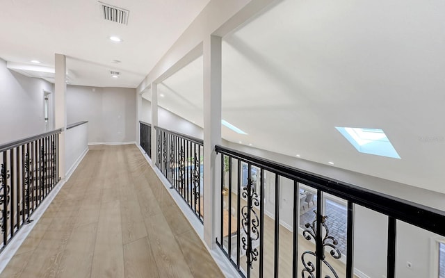 corridor with light hardwood / wood-style floors and vaulted ceiling with skylight