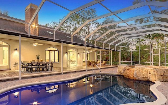 pool at dusk with glass enclosure, ceiling fan, and a patio area