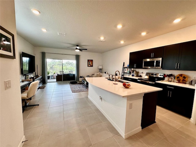 kitchen with stainless steel appliances, ceiling fan, sink, light tile patterned floors, and a center island with sink