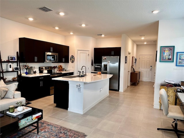 kitchen featuring a kitchen island with sink, sink, a textured ceiling, light tile patterned flooring, and stainless steel appliances