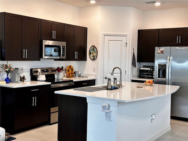 kitchen featuring dark brown cabinets, an island with sink, stainless steel appliances, and light tile patterned floors