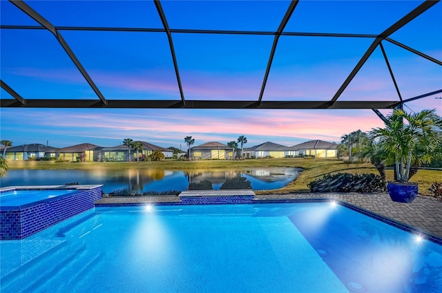 pool at dusk featuring a lanai, a water view, and an in ground hot tub