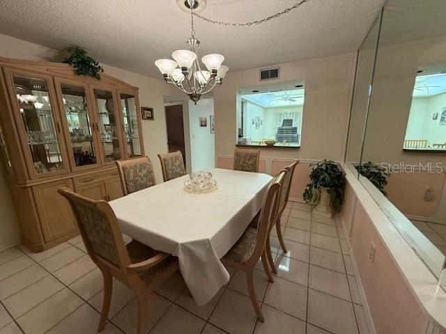 tiled dining room with a textured ceiling and a chandelier