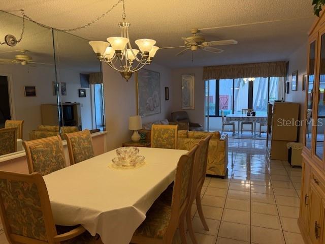 tiled dining room with ceiling fan with notable chandelier and a textured ceiling