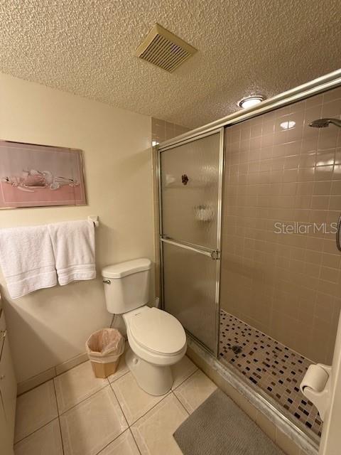 bathroom featuring tile patterned flooring, a textured ceiling, toilet, and walk in shower