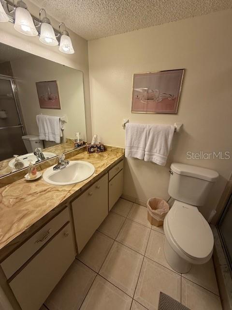 bathroom featuring walk in shower, tile patterned floors, a textured ceiling, toilet, and vanity