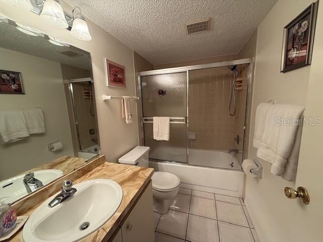 full bathroom featuring tile patterned flooring, a textured ceiling, toilet, and enclosed tub / shower combo