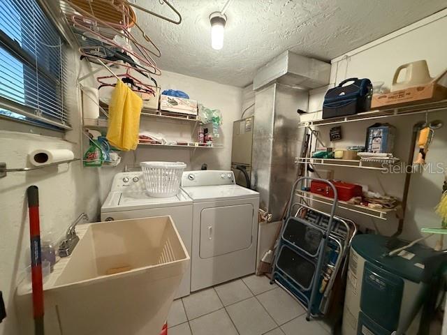 clothes washing area featuring light tile patterned floors, a textured ceiling, separate washer and dryer, and sink