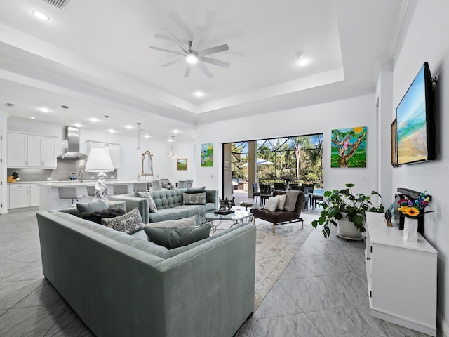 living room with ceiling fan, a raised ceiling, and sink