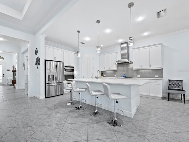 kitchen featuring appliances with stainless steel finishes, a kitchen breakfast bar, a kitchen island with sink, wall chimney range hood, and hanging light fixtures