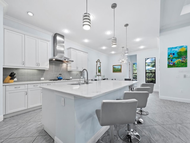 kitchen featuring a center island with sink, wall chimney exhaust hood, pendant lighting, and white cabinetry