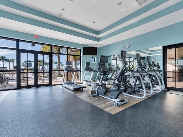 workout area with a raised ceiling and french doors