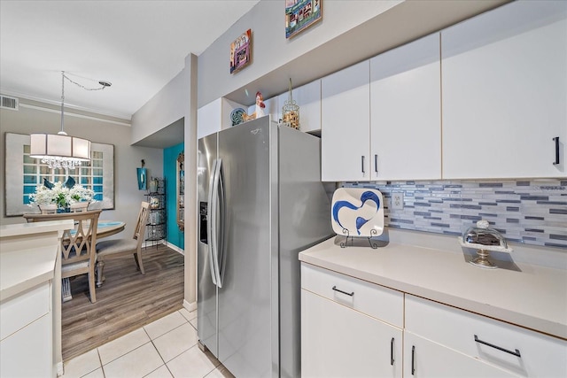 kitchen with light wood-type flooring, crown molding, stainless steel fridge with ice dispenser, white cabinetry, and hanging light fixtures